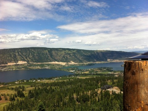 Scenic view of a lake, mountains, and cloudy sky from a hilltop.