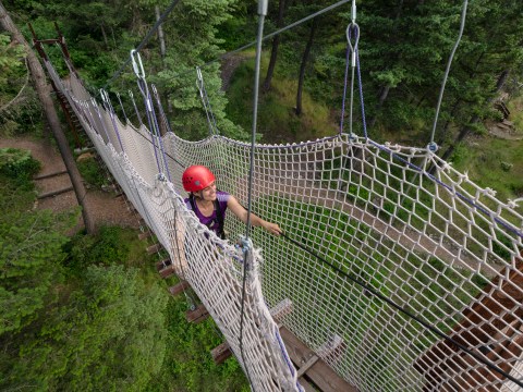 Person with a red helmet crossing a rope bridge in a forest.