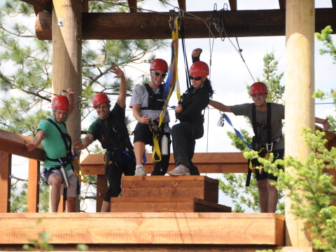 Five people in helmets and harnesses pose on a zipline platform.