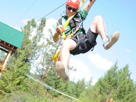 Person ziplining with helmet and harness, smiling over green forest.