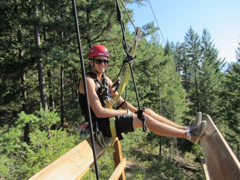 Person in helmet and harness zip-lining over a forested area.