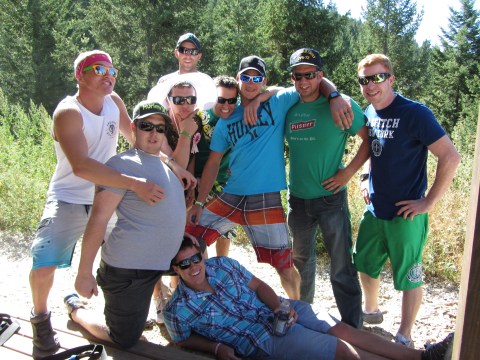Group of men posing outdoors in casual wear, surrounded by trees.