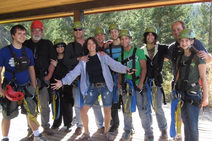 Group of people wearing helmets and harnesses, posing outdoors on a wooden deck with trees in the background.