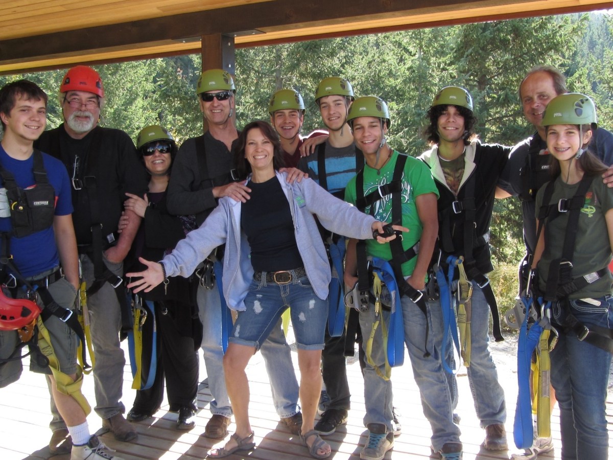 Group of people wearing helmets and harnesses, posing outdoors on a wooden deck with trees in the background.