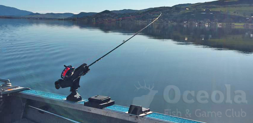 Fishing rod on boat, calm lake, and distant hills.