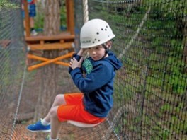 Child wearing a helmet on a rope swing in a forest adventure course.