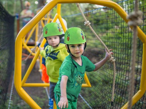 Two kids wearing helmets navigate a ropes course.